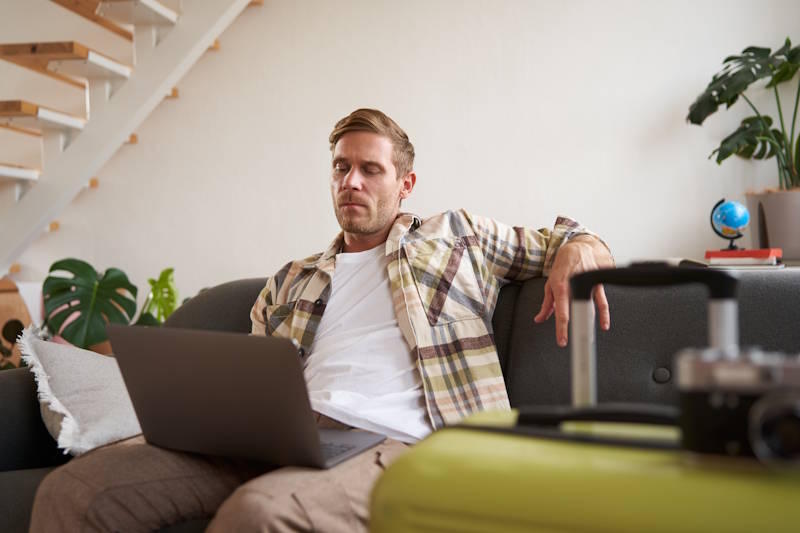 Man sitting on a sofa with a laptop, looking thoughtful and withdrawn, reflecting on relationship communication difficulties and emotionally draining conversations.